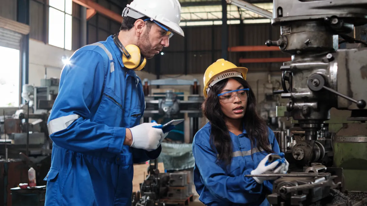 Manufacturing workers with proper PPE discussing work on factory floor